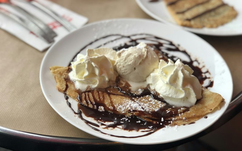 A golden crepe folded on a plate with ice cream and syrup